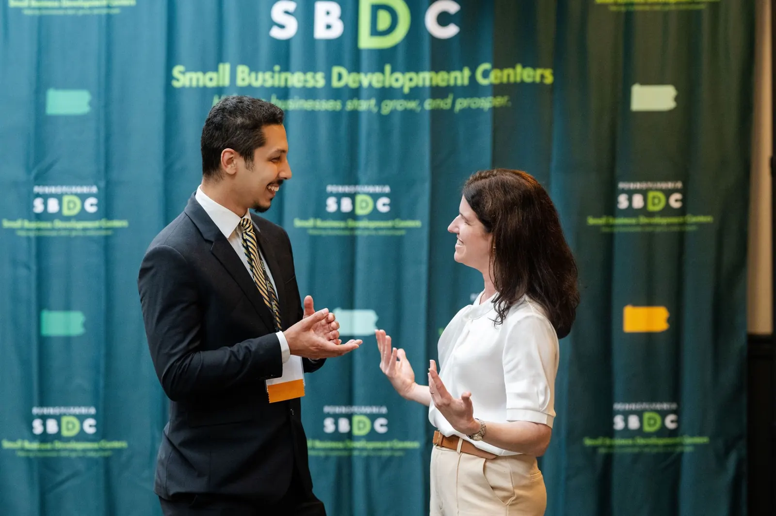 Two SBDC attendees in conversation in front of a Pennsylvania SBDC backdrop